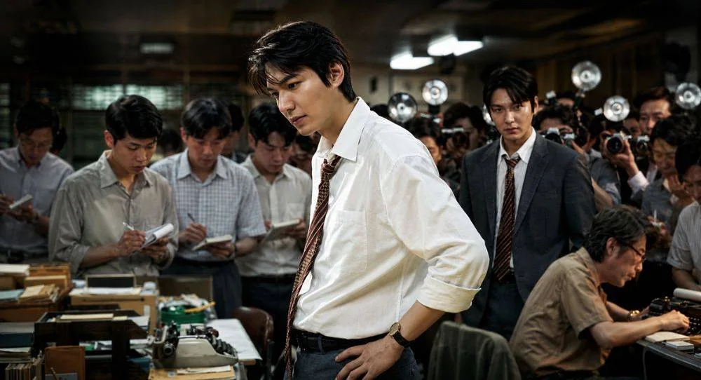 Lee Min Ho appears at a tense press conference as a rookie reporter who witnesses a historic shooting and risks everything to uncover the truth in 'Assassins'